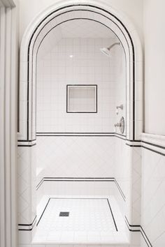 a bathroom with white tile and black trim on the shower wall, along with an arched doorway