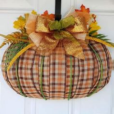 a plaid pumpkin hanging on the front door with a bow and autumn decorations around it