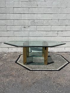 a glass table sitting on top of a cement floor next to a white brick wall