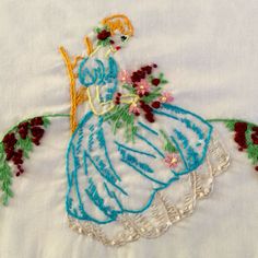 an embroidered piece of cloth with a woman in a blue dress and flowers on it