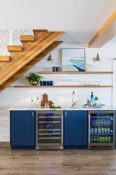 a kitchen with blue cabinets and stairs in the background, along with an under counter beverage cooler