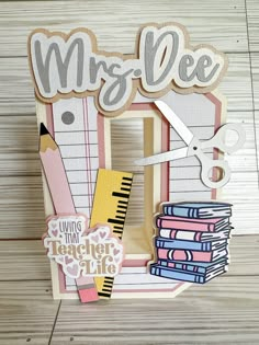 a close up of a wooden frame with scissors and books on it that says mrs mee