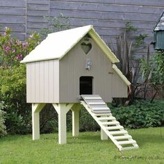 a dog house with stairs leading up to the roof and door open, in front of a garden