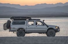 a pick up truck parked on the side of a body of water with mountains in the background