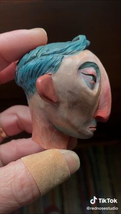 a hand holding a clay sculpture of a man with blue hair