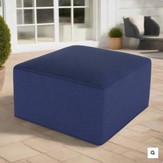 a large blue ottoman sitting on top of a brick floor next to a potted plant