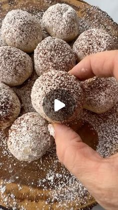 a person is holding some powdered doughnuts on a wooden platter with sprinkles