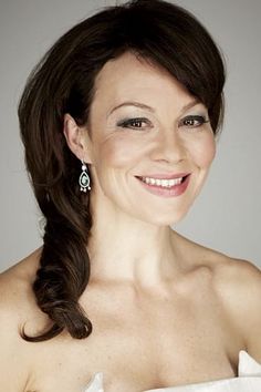 a woman in a white dress smiling at the camera with her hair pulled back and wearing earrings