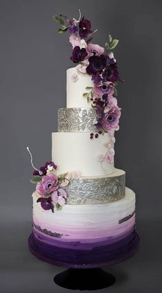 a three tiered cake with purple flowers on the top and silver trimmings