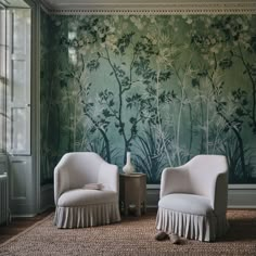 two white chairs sitting in front of a green wallpapered room with trees on it