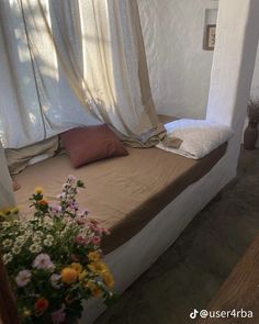 a bed sitting under a window next to a vase with flowers