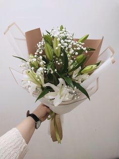 a bouquet of flowers is being held by a woman's hand with white lilies