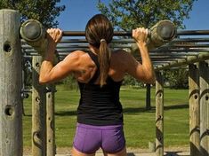 a woman in purple shorts and black tank top holding two dumbbells behind her back