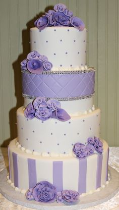 a three tiered cake with purple flowers on the top and bottom, sitting on a table