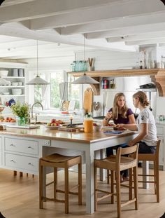 two people sitting at a kitchen island in a large white kitchen with wood floors and cabinets