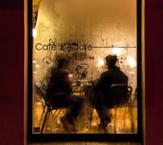 two people sitting at a table in front of a window with the words cafe adore written on it