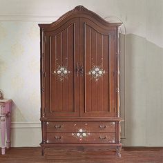 a wooden armoire sitting on top of a hard wood floor next to a pink chair