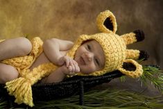 a baby wearing a yellow crocheted hat laying on top of a black basket