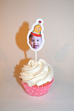 a cupcake with white frosting and a birthday hat on top is shown in front of a shadow