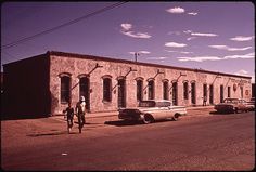 an old brick building with cars parked on the side and people walking down the street