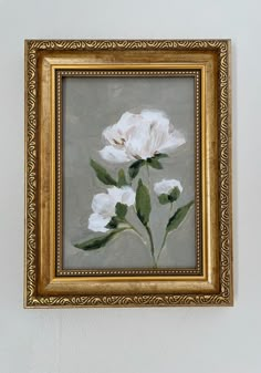 a painting of white flowers in a gold frame hanging on a wall with a gray background