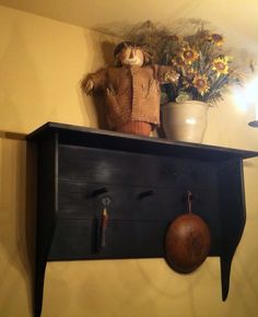 a wooden shelf with an old fashioned doll on top and a potted plant behind it