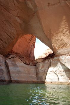 an arch in the side of a rock formation over water with people standing on it