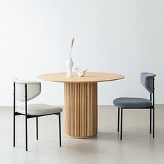 two chairs and a table with a vase on it in front of a white wall