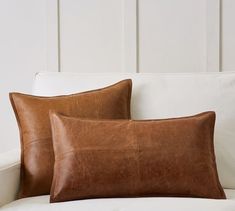 two brown leather pillows sitting on top of a white couch