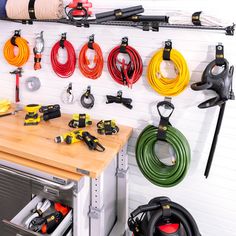 a workbench with various tools hanging on the wall and below it is an assortment of hoses