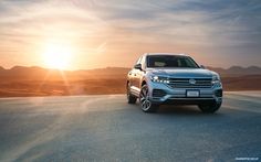 the volkswagen cayen is parked on the side of the road with the sun setting in the background