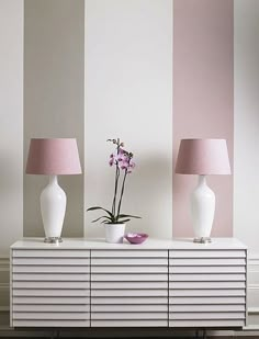 two white vases with pink lamps on top of a dresser in a living room