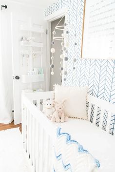 a white crib with a teddy bear on it in a room that has blue and white wallpaper