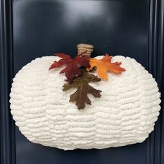 a knitted pumpkin with fall leaves on it's side hanging from the front door