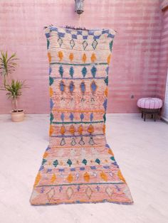 an old rug is sitting on the floor in front of a pink wall and potted plant