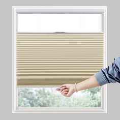 a woman standing in front of a window with her hand on the side of the blind