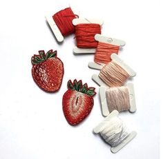 several spools of thread and two strawberries on a white surface with one red strawberry in the center