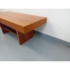 a wooden table sitting on top of a floor next to a white wall and gray floor