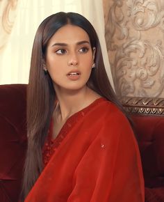 a woman sitting on top of a red couch wearing a red dress and diamond earrings