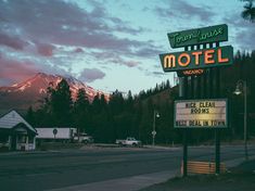 a motel sign sitting on the side of a road next to a forest covered mountain