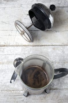 a cup of coffee sitting on top of a wooden table next to a strainer