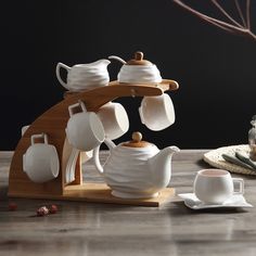 a tea set on a wooden table with cups and saucers next to the coffee pot