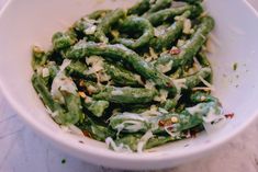 a white bowl filled with green beans covered in cheese and seasoning sitting on top of a marble counter