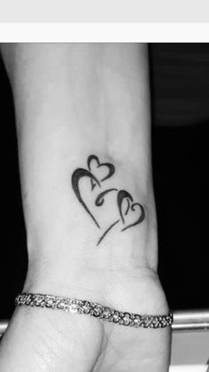 two hearts tattoo on the wrist with an arrow in the shape of a couple's initials