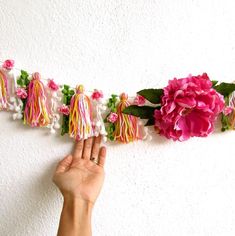 a hand is reaching for some flowers on a string that has tassels attached to it