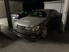 a silver car parked in front of a garage with other cars behind it at night