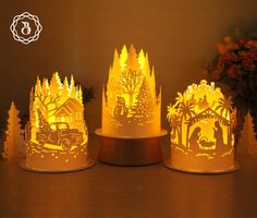 three paper lamps with trees and houses on them, one is lit up in the dark