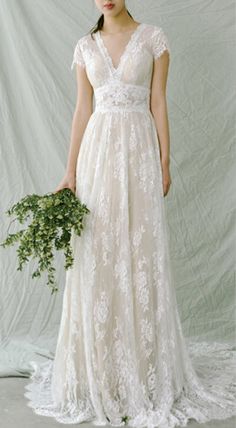 a woman in a white wedding dress holding a green plant and posing for the camera