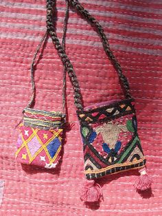 two small purses are hanging on a pink cloth with tassels and beads