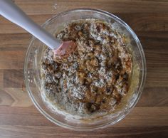 a glass bowl filled with food on top of a wooden table next to a plastic spoon